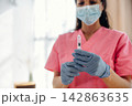 Healthcare professional in pink scrubs holds a syringe filled with insulin, wearing blue gloves and a face mask, in a well-lit clinical environment with soft natural light 142863635