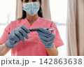 Healthcare professional in pink scrubs wearing gloves and a mask holds an insulin pen for diabetes management in a well-lit medical environment 142863638