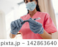 Healthcare professional in pink scrubs prepares insulin syringe for diabetes treatment, wearing blue gloves and a surgical mask in a clinical setting with natural light 142863640