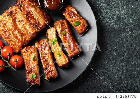 Hot grilled spare ribs from a summer BBQ served on a plate with sauce. Top view. Copy space Hot grilled spare ribs from a summer BBQ served on a plate with sauce. Top view. Copy space 142863779