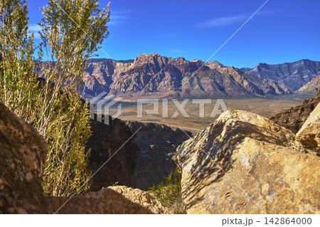 Red Rock Canyon Desert Landscape with Sunlit Boulders and Distant Mountains Red Rock Canyon Desert Landscape with Sunlit Boulders and Distant Mountains 142864000