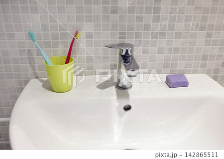 White ceramic sink with chrome faucet and plastic cup containing toothbrushes. 142865511