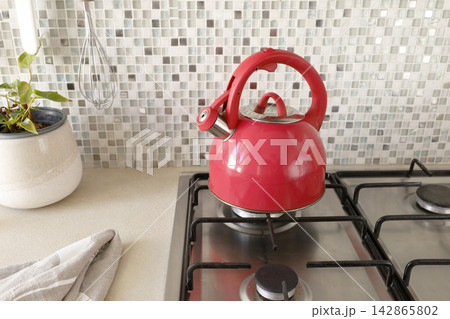 Red whistling kettle standing on stainless steel gas stove top. Red whistling kettle standing on stainless steel gas stove top. 142865802