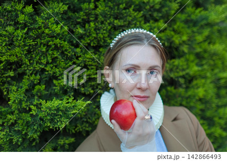 Woman holding red apple by green hedge Woman holding red apple by green hedge 142866493