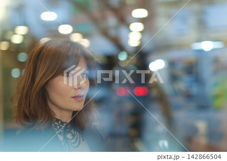 Woman looking through glass window in urban setting Woman looking through glass window in urban setting 142866504