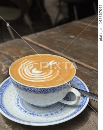 Fresh hot cafe latte with delicate heart latte art served in a traditional Chinese porcelain teacup and saucer on a rustic wooden table at a cafe in Hong Kong 142867045