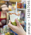 Hand holding a cup of traditional Vietnamese avocado coconut smoothie (Sinh To Bo) topped with crispy toasted coconut chips at a local market in Da Nang, Vietnam 142867046