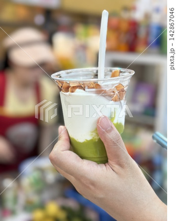 Hand holding a cup of traditional Vietnamese avocado coconut smoothie (Sinh To Bo) topped with crispy toasted coconut chips at a local market in Da Nang, Vietnam 142867046