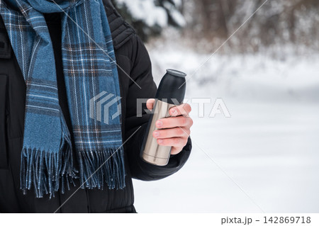Young adult man holding thermos in winter park 142869718