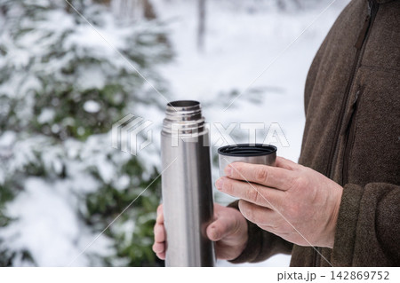 Man holding stainless steel thermos cup outdoors in winter forest Man holding stainless steel thermos cup outdoors in winter forest 142869752