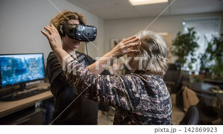 Senior woman experiencing virtual reality therapy with caregiver 142869923