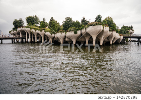 Close up of Little Island's unique concrete tulip shaped pillars rising above the Hudson River in Manhattan. Lush greenery and modern architecture create a striking urban waterfront landmark. Close up of Little Island's unique concrete tulip shaped pillars rising above the Hudson River in Manhattan. Lush greenery and modern architecture create a striking urban waterfront landmark. 142870298