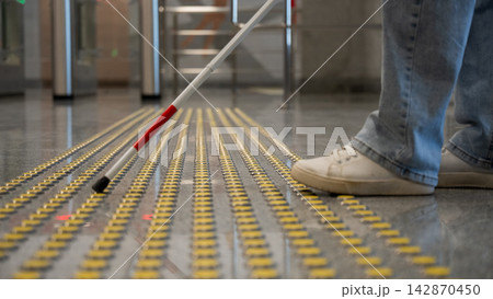 A blind woman walks on tactile paving. Close-up of her feet and a walking stick. 142870450