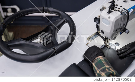 A seamstress in a workshop makes a new leather cover for a car steering wheel. 142870508