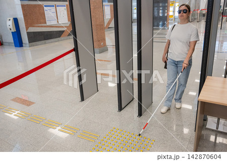 A blind woman walks through a metal detector. A blind woman walks through a metal detector. 142870604