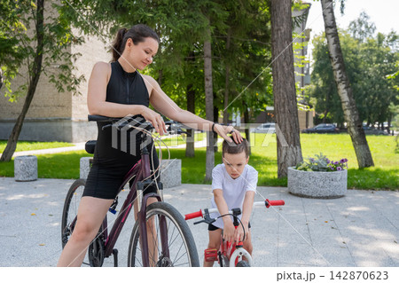 A Caucasian woman is riding a bicycle with her son. The boy fell, and the mother feels sorry for him. A Caucasian woman is riding a bicycle with her son. The boy fell, and the mother feels sorry for him. 142870623