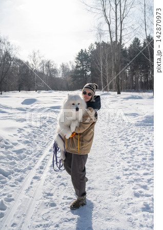 Smiling woman holding fluffy samoyed dog in snowy winter park. Smiling woman holding fluffy samoyed dog in snowy winter park. 142870973