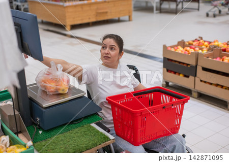 A Caucasian woman in a wheelchair buys fruit at a supermarket. A Caucasian woman in a wheelchair buys fruit at a supermarket. 142871095