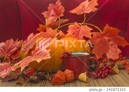 Autumn still life; mug of tea; orange squash and dry leaves on a wooden background Autumn still life; mug of tea; orange squash and dry leaves on a wooden background 142871101