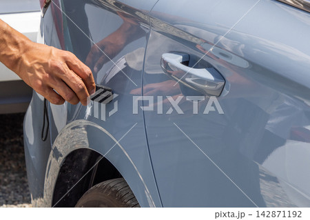 Adult Hand Touching Gray Car with Black Thickness Metering Device 142871192