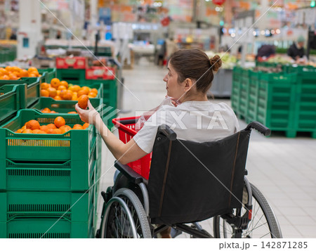 A Caucasian woman in a wheelchair buys fruit at a supermarket. A Caucasian woman in a wheelchair buys fruit at a supermarket. 142871285