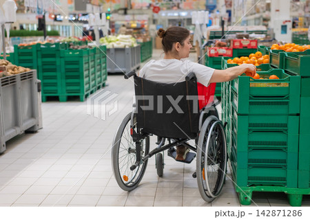 A Caucasian woman in a wheelchair buys fruit at a supermarket. A Caucasian woman in a wheelchair buys fruit at a supermarket. 142871286