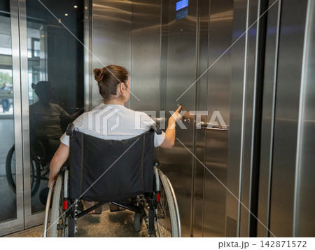 A Caucasian woman in a wheelchair uses an elevator. A Caucasian woman in a wheelchair uses an elevator. 142871572