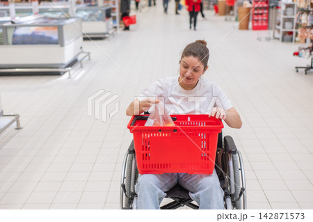 A Caucasian woman in a wheelchair buys fruit at a supermarket. A Caucasian woman in a wheelchair buys fruit at a supermarket. 142871573