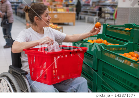 A Caucasian woman in a wheelchair buys fruit at a supermarket. 142871577