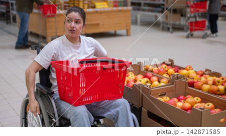 A Caucasian woman in a wheelchair buys apples at a supermarket. A Caucasian woman in a wheelchair buys apples at a supermarket. 142871585