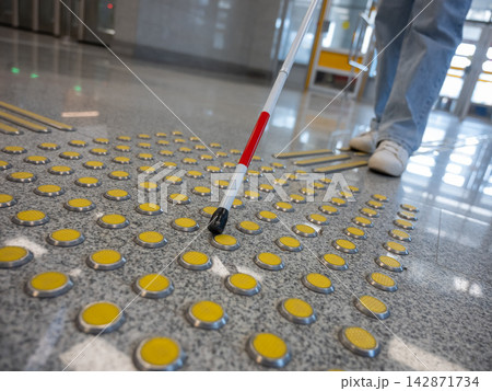 A blind woman walks on tactile paving. Close-up of her feet and a walking stick. A blind woman walks on tactile paving. Close-up of her feet and a walking stick. 142871734