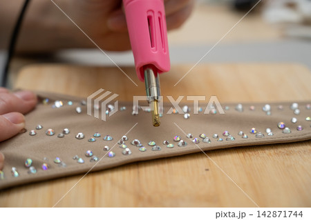 A woman glues rhinestones onto a gymnastics costume using a soldering iron. Hot fix. 142871744