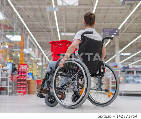 A Caucasian woman in a wheelchair shopping in a supermarket. A Caucasian woman in a wheelchair shopping in a supermarket. 142871754