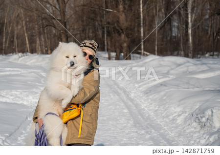 Smiling woman holding fluffy samoyed dog in snowy winter park. Smiling woman holding fluffy samoyed dog in snowy winter park. 142871759