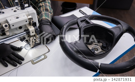 A seamstress in a workshop makes a new leather cover for a car steering wheel. 142871931