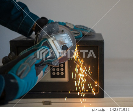 A man breaks into a safe with a grinder. A man breaks into a safe with a grinder. 142871932
