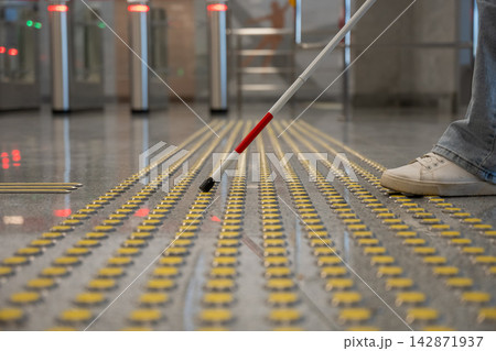 A blind woman walks on tactile paving. Close-up of her feet and a walking stick. 142871937