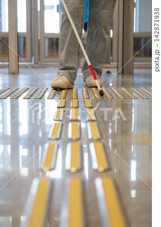 A blind woman walks on tactile paving. Close-up of her feet and a walking stick. 142871938