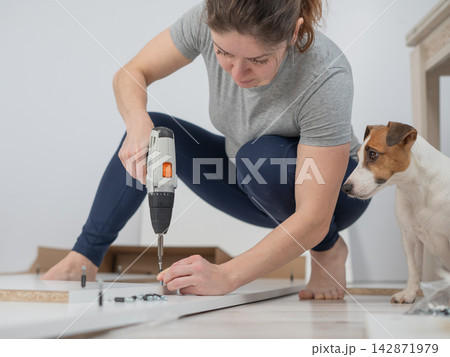 A Caucasian woman uses a screwdriver to tighten a screw while assembling a cabinet. 142871979