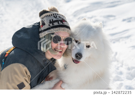 Portrait of a Smiling woman holding fluffy samoyed dog in snowy winter park. Portrait of a Smiling woman holding fluffy samoyed dog in snowy winter park. 142872235