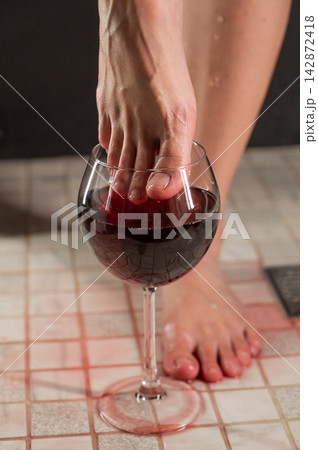 Foot fetish. A woman dips her toes in a glass of red wine. 142872418