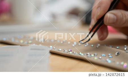 A woman decorates a gymnastics costume with rhinestones. Rhythmic gymnastics. Arranging with tweezers. 142872615
