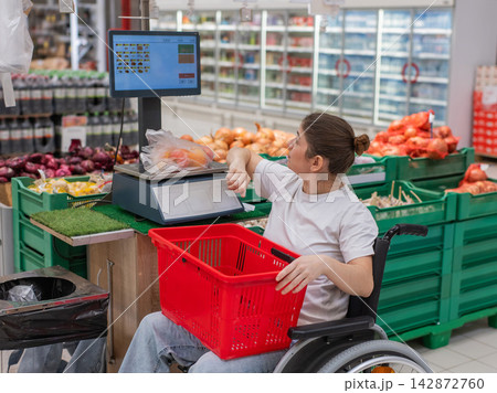 A Caucasian woman in a wheelchair buys fruit at a supermarket. A Caucasian woman in a wheelchair buys fruit at a supermarket. 142872760