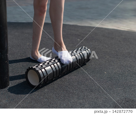 A Caucasian woman uses a foam roller to stretch her feet on a sports field. Close-up of her feet. A Caucasian woman uses a foam roller to stretch her feet on a sports field. Close-up of her feet. 142872770