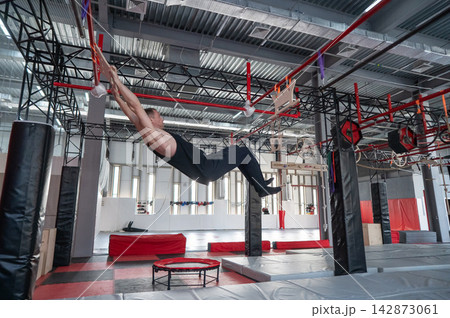 An athletic man practices at a ninja club's indoor obstacle course. 142873061