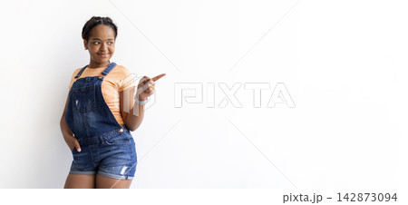 Smiling Black teenage girl pointing toward copy space, standing against white background Smiling Black teenage girl pointing toward copy space, standing against white background 142873094