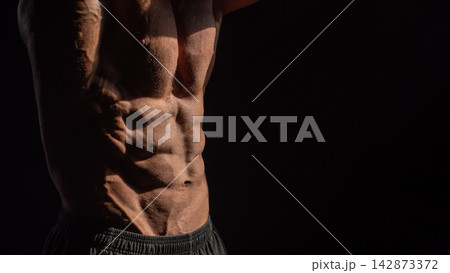 A male bodybuilder poses in shorts, showing off his muscles. Close-up of his chest and abs. A male bodybuilder poses in shorts, showing off his muscles. Close-up of his chest and abs. 142873372