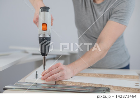 A Caucasian woman uses a screwdriver to tighten a screw while assembling a cabinet. 142873464