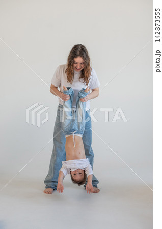 A Caucasian woman holds her two-year-old son by the legs. The boy and mother are playing around. A Caucasian woman holds her two-year-old son by the legs. The boy and mother are playing around. 142873555