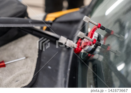 A technician injects resin into a windshield crack. A technician injects resin into a windshield crack. 142873667